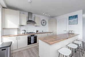Eine moderne Küche mit weißen Schränken, einer Holz Arbeitsplatte, einem Gasherd, einer Kaffeemaschine und einer Uhr.