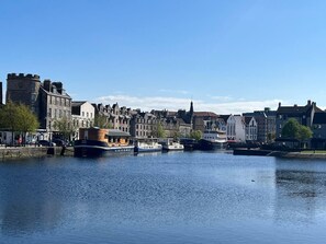 Stadtsilhouette am Wasser mit historischen Gebäuden, einem Fluss und Booten.