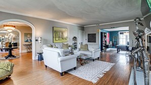 A spacious living room with hardwood floors, white sofas, a coffee table, and a chandelier. - Historic Group Retreat w/ Pool in Paducah (Paducah)