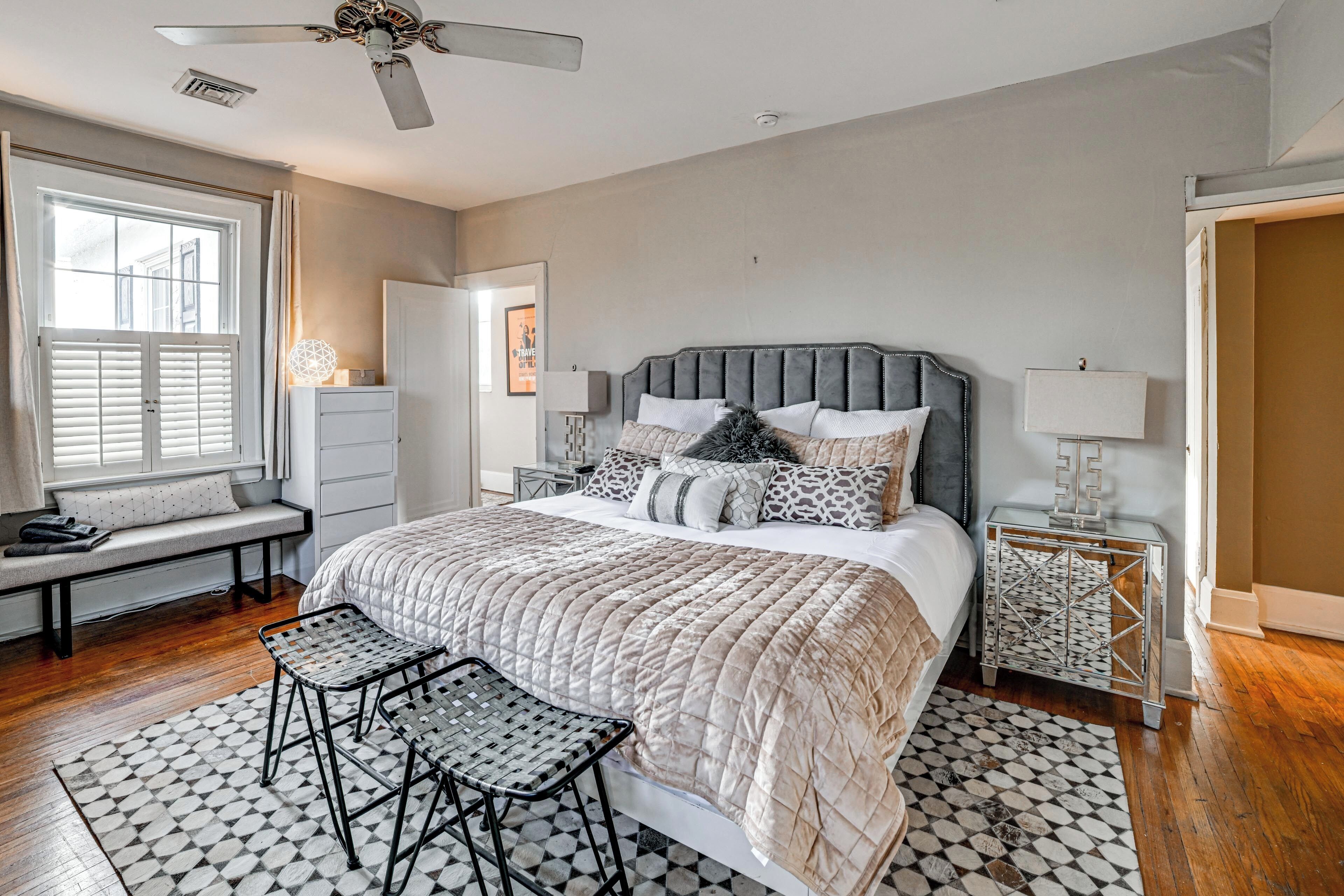 A bedroom with a bed, a bench, a small table, a ceiling fan, and a window.