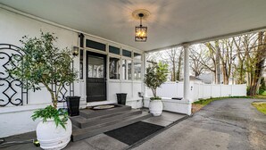 A covered porch with steps leading to a door, potted plants, and a white fence. - Historic Group Retreat w/ Pool in Paducah (Paducah)