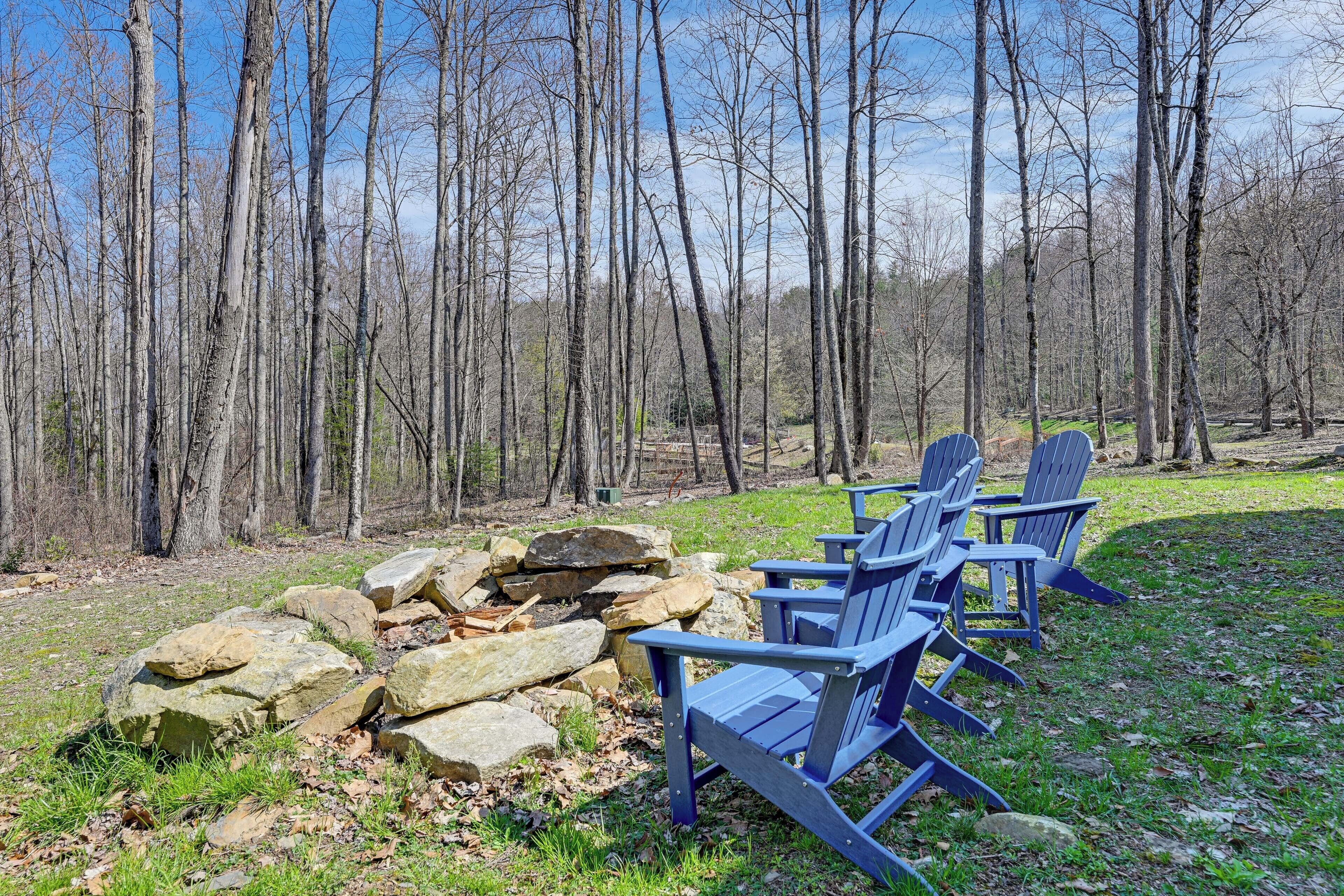 A row of Adirondack chairs near a stone wall in a forested area.