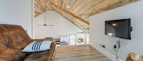 A living room with a brown leather couch, a television mounted on the wall, and a wooden ceiling.