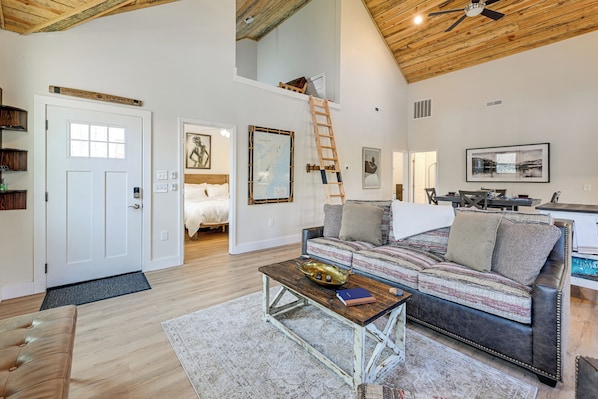 A spacious living area with a loft bedroom, a wooden ceiling, a sofa, a coffee table, and a ladder. - Fire Pit w/ Pond: Modern Mtn Retreat in Smoky Mtns (Andrews)