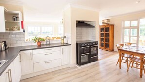 A modern kitchen with white cabinetry, a black stove, and a wooden dining table. - 3 Lovely Cornish Cottages near Bude - Sleeps 21 (Bude)