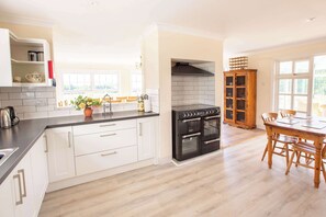 A modern kitchen with white cabinetry, a black stove, and a wooden dining table. - 3 Lovely Cornish Cottages near Bude - Sleeps 21 (Bude)