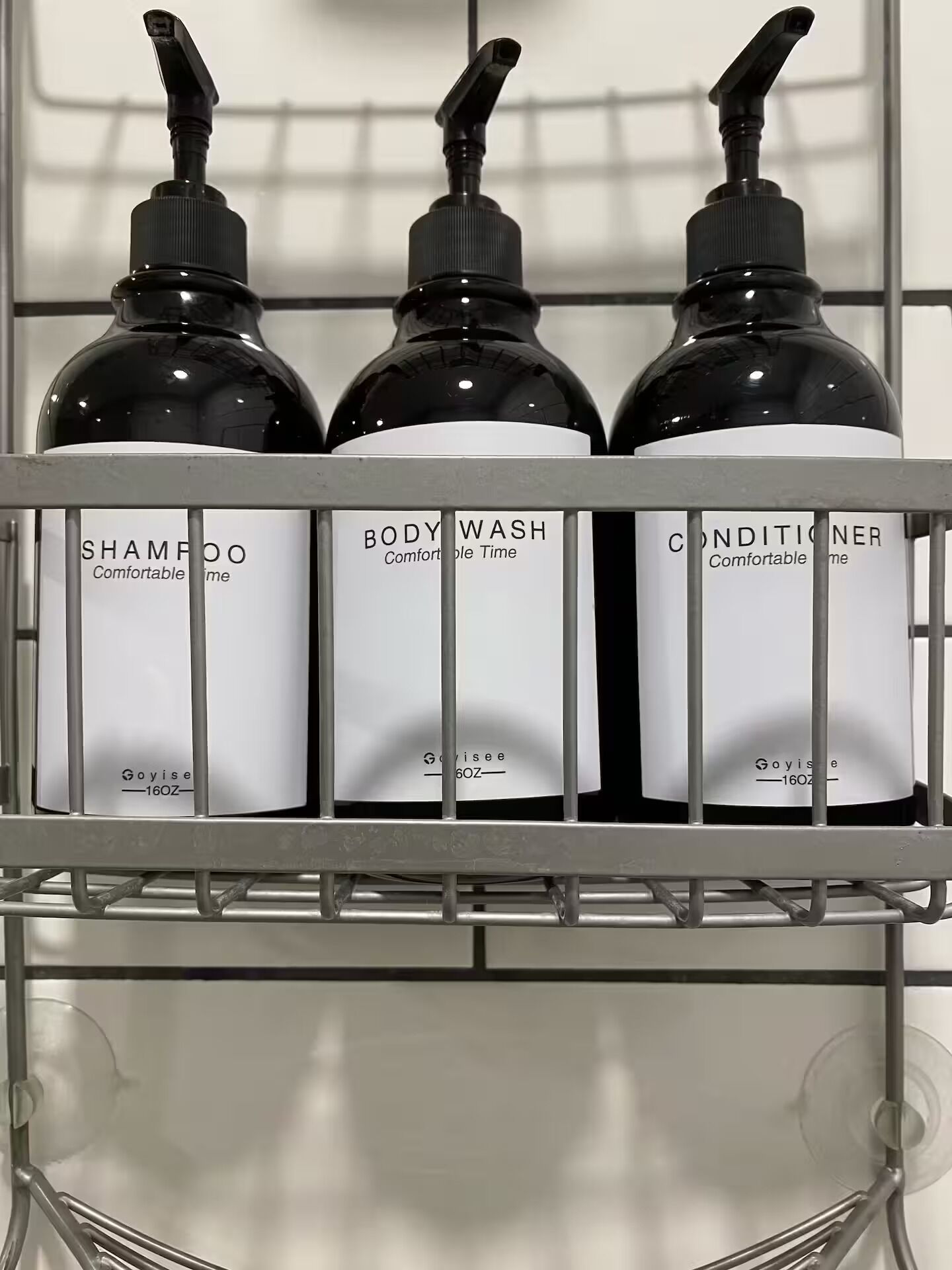 A metal shelf with three bottles of personal care products labeled 'Shampoo,' 'Body Wash,' and 'Conditioner,' each with a pump dispenser.