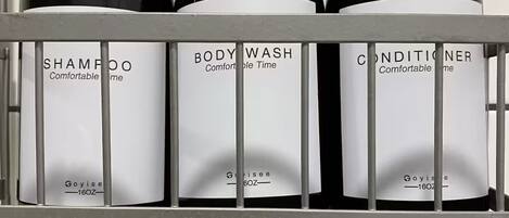 A metal shelf with three bottles of personal care products labeled 'Shampoo,' 'Body Wash,' and 'Conditioner,' each with a pump dispenser.