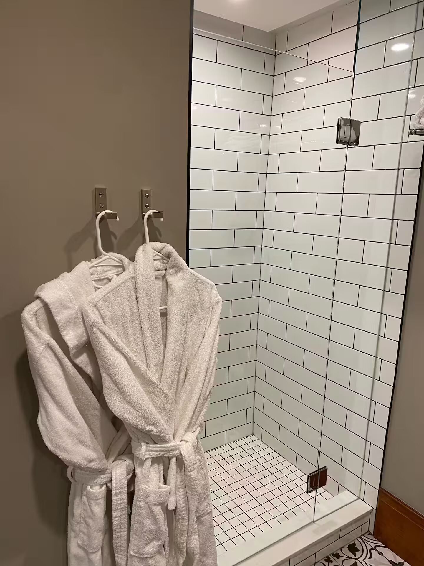 Een douche met witte betegelde wanden en een vloer met een rasterpatroon.