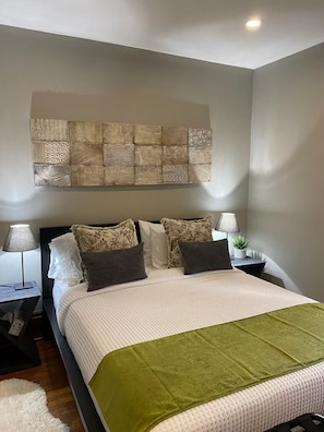 Ein ordentlich eingerichtetes Schlafzimmer mit Bett, Kissen, Nachttisch, Lampe und einem Wandbild.