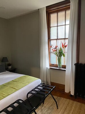 A bedroom with a bed, a nightstand, a window with curtains, and a potted plant.