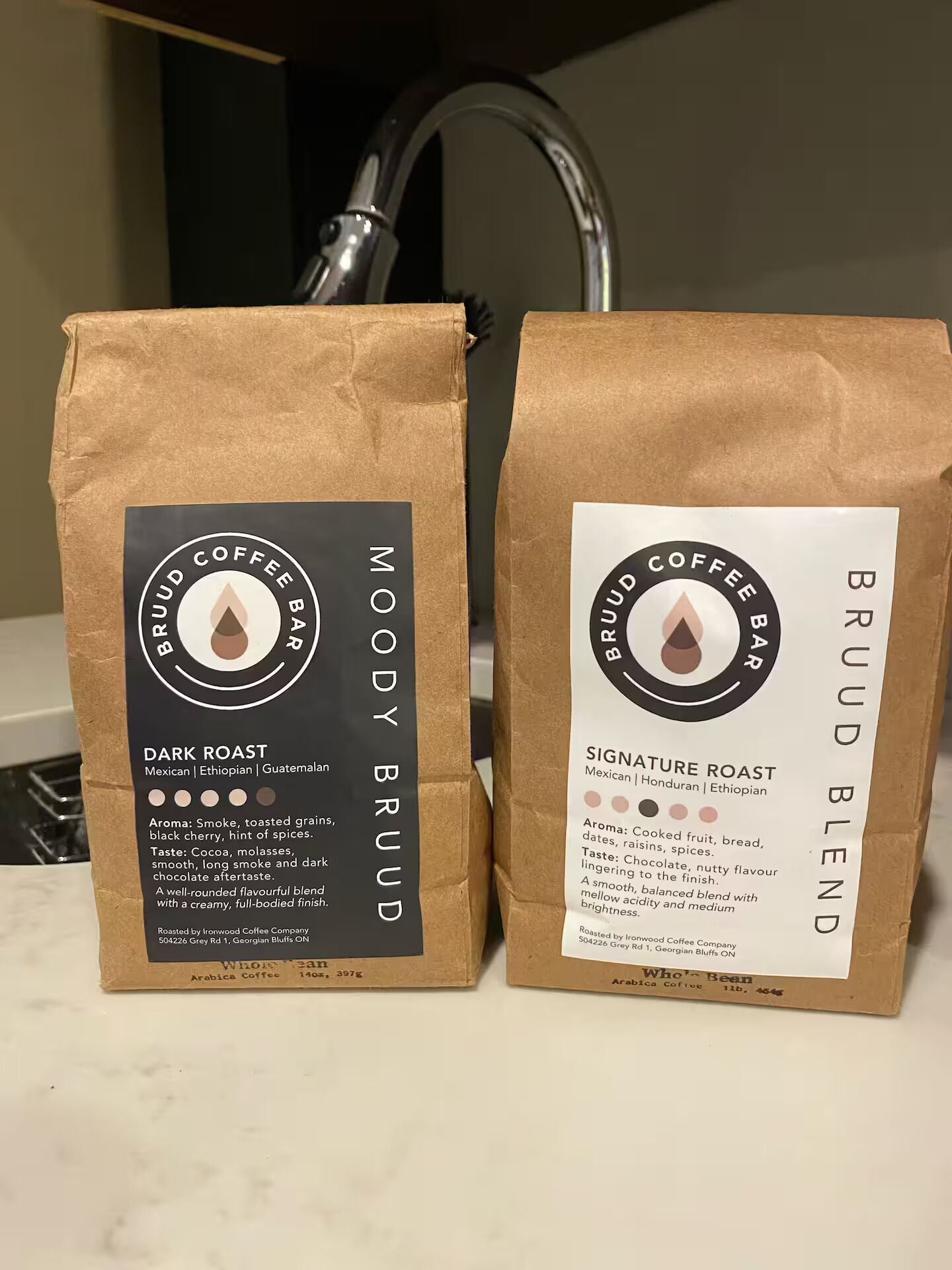 Two coffee bags labeled 'Moody Brud' and 'Signature Roast Blend' with roast types and origin details.