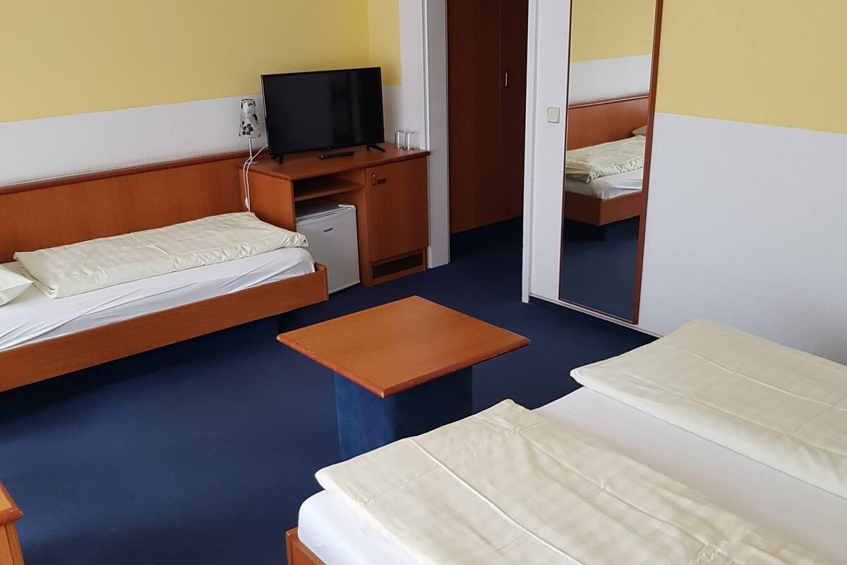 Hotellihuone, jossa on kaksi sänkyä, pieni työpöytä, televisio ja peili.