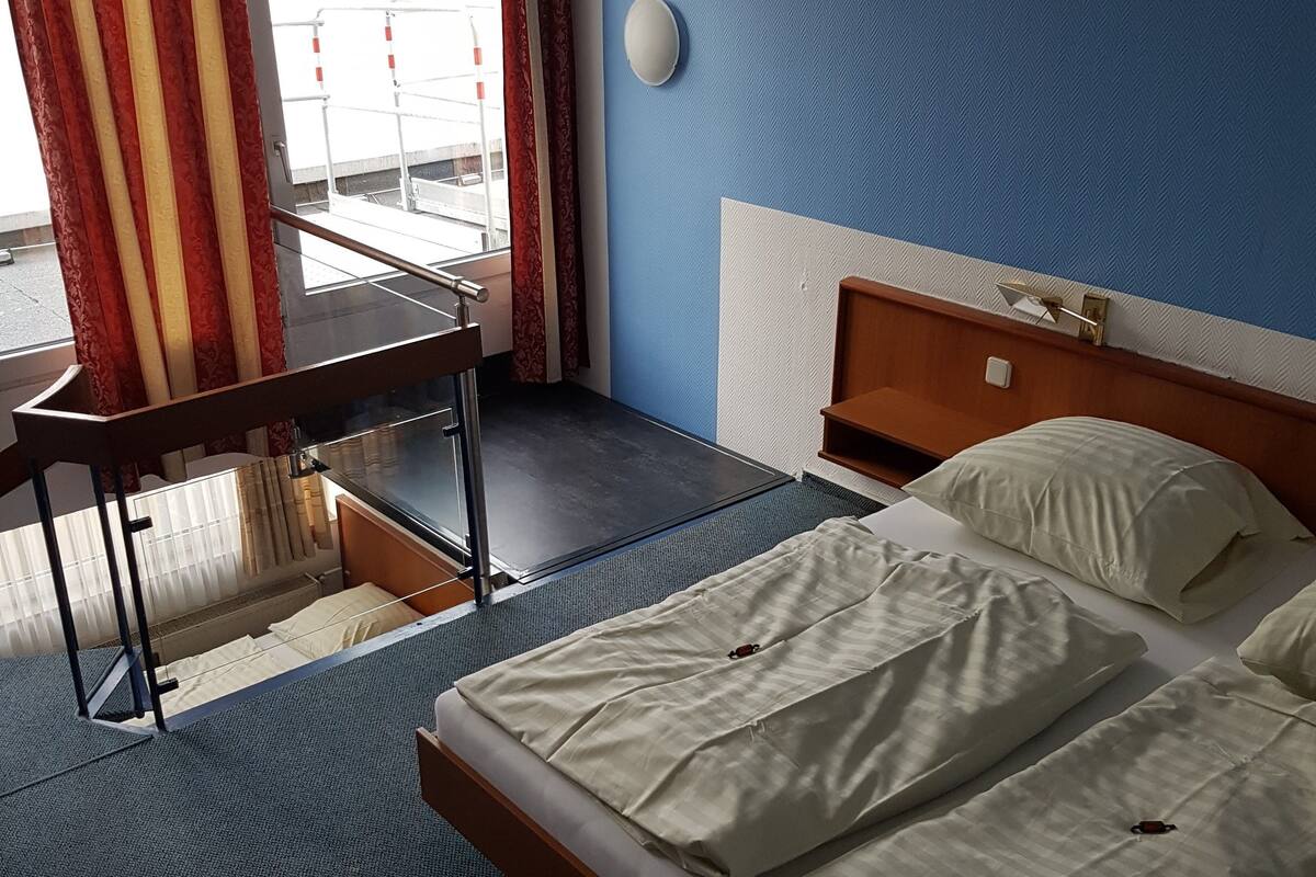 Hotellihuone, jossa on sänky, työpöytä ja ikkuna, jossa on verhot.
