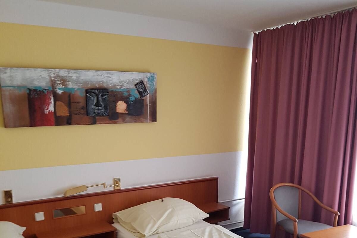 Hotellihuone, jossa on kaksi erillistä sänkyä, puinen pääty, pieni pöytä, tuoli ja seinälle ripustettu taideteos.