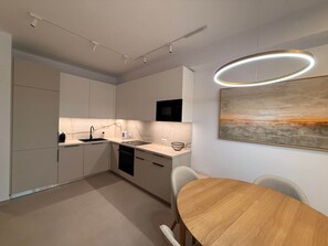 A modern kitchen with white cabinetry, a wooden dining table, and a contemporary pendant light. - Arletta - Panoramic View (Sarandë)