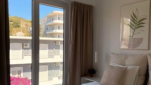 Habitación de hotel con cama, ventana con cortinas, un cuadro en la pared y vistas a edificios.