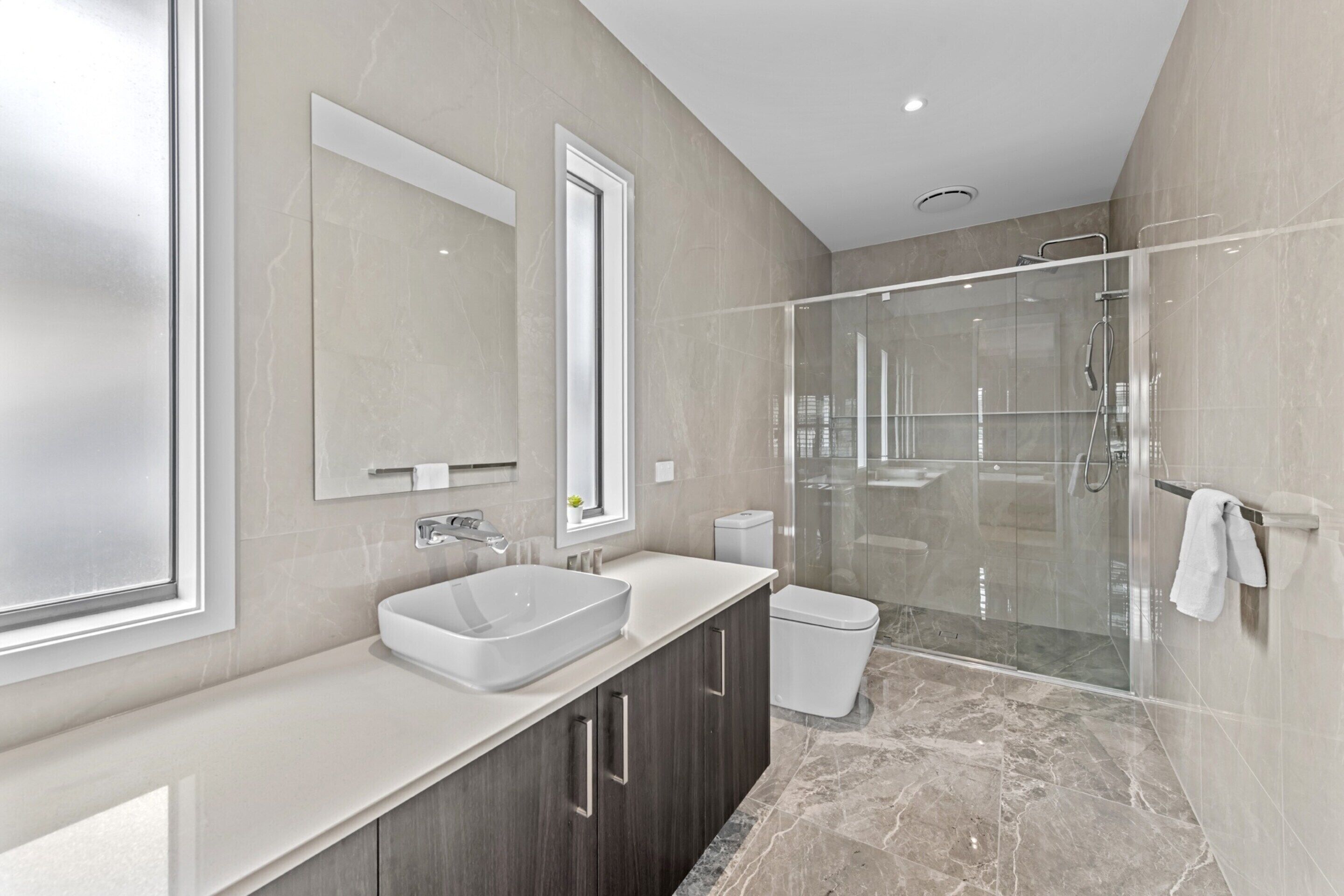A modern bathroom with a large mirror, a sink, a toilet, and a glass-enclosed shower area.