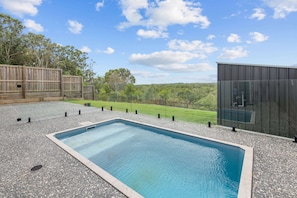 A rectangular pool with a clear blue water surface, surrounded by a pebble surface and a wooden fence. - Brand New Riverfront Home, Pool and Sunrise Views (Griffin)