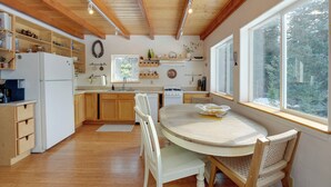 A kitchen with wooden cabinets, a dining table, and a view of trees outside. - Secluded Homer Escape With Deck in Quite Woods (Homer)