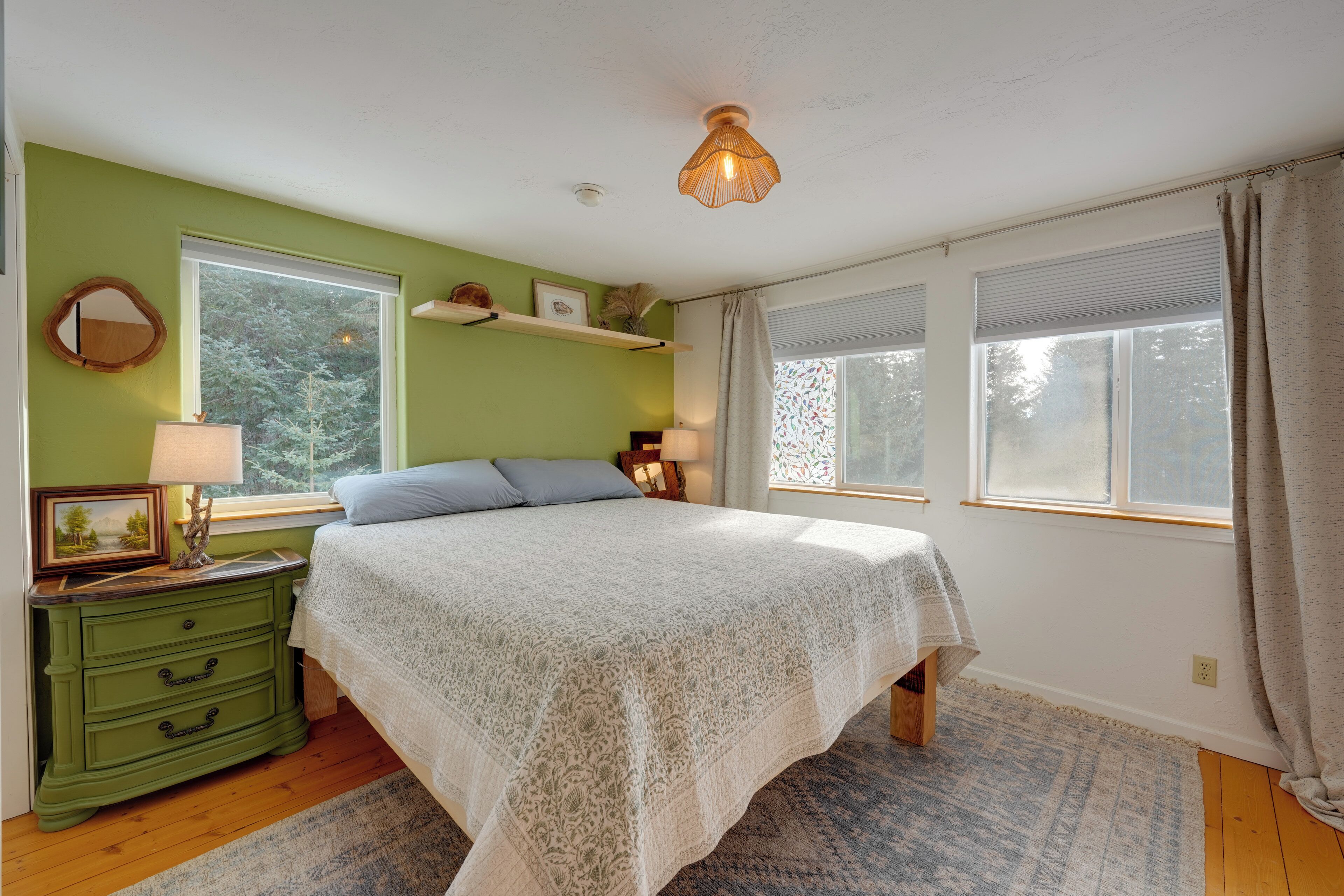 A bedroom with a bed, dresser, bedside lamps, and a window with curtains.