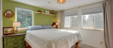 A bedroom with a bed, dresser, bedside lamps, and a window with curtains.