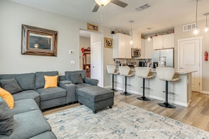 A modern living room with a sectional sofa, ottoman, and a bar area with stools. - Explore, Shop & Relax! Getaway in West Sacramento (West Sacramento)