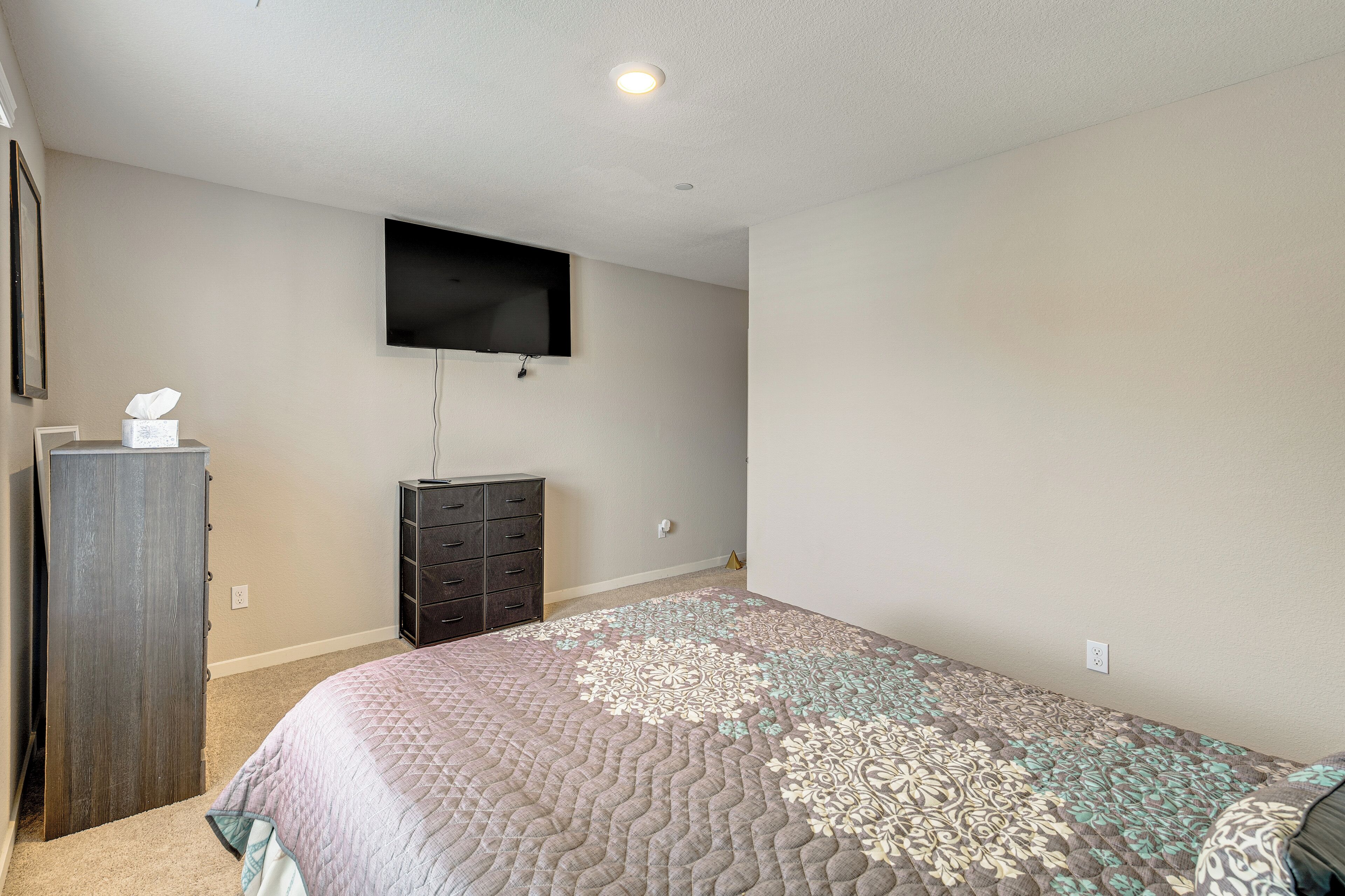 Une chambre à coucher comprenant un lit, une commode, un téléviseur fixé au mur et un sol recouvert de moquette.