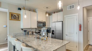 A kitchen with white cabinets, a granite countertop, a stainless steel refrigerator, and a bar stool area. - Explore, Shop & Relax! Getaway in West Sacramento (West Sacramento)