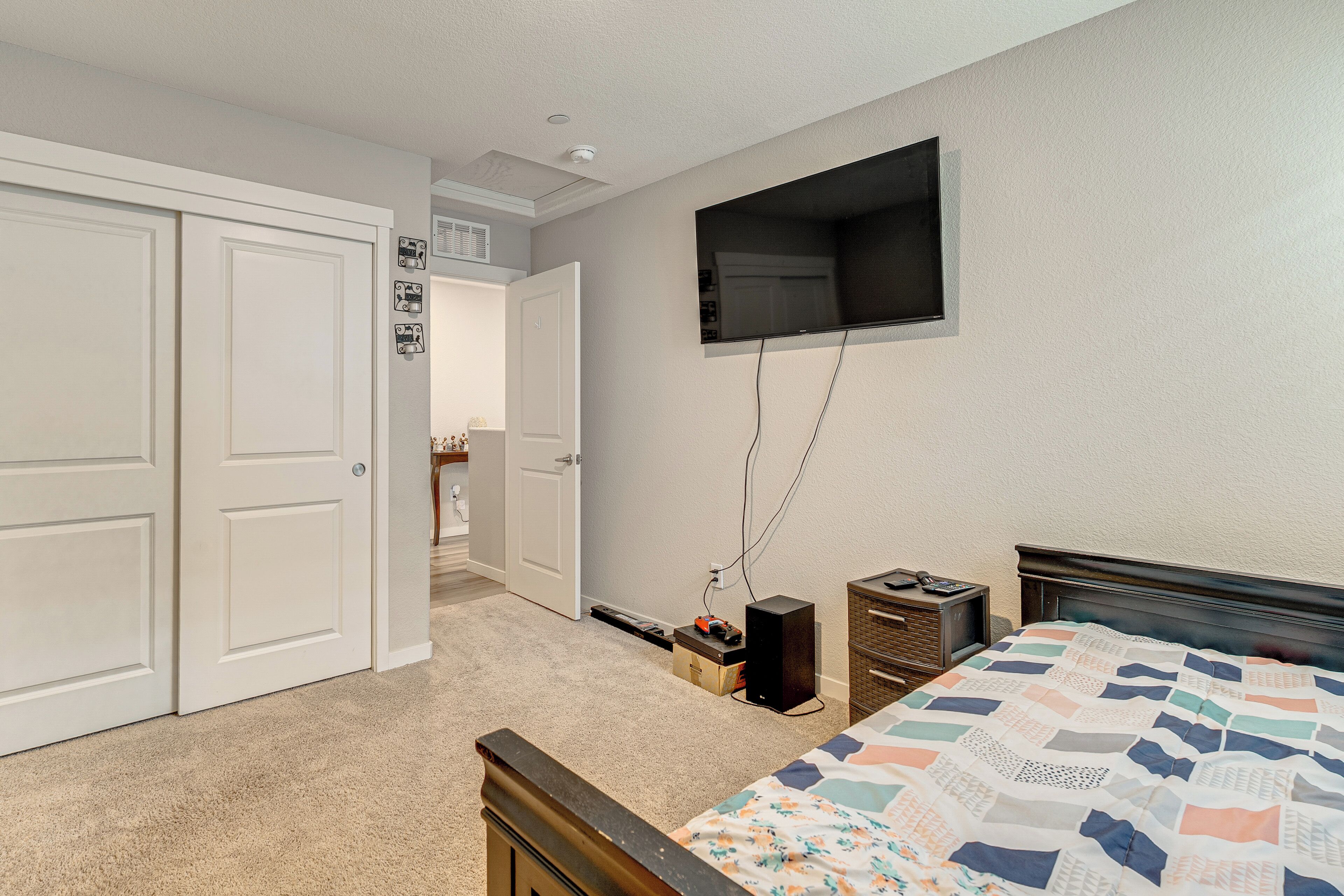 A bedroom with a bed, a TV mounted on the wall, a door, and a carpeted floor.