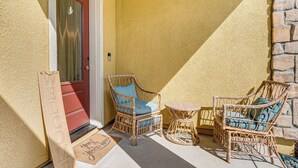 Une chaise en osier avec un coussin, une petite table ronde et un panneau d’accueil sur un porche.
