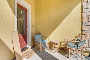 Une chaise en osier avec un coussin, une petite table ronde et un panneau d’accueil sur un porche.