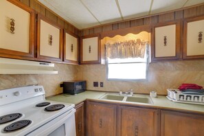 A kitchen with wooden cabinets, a white stove, a microwave, and a window with curtains.