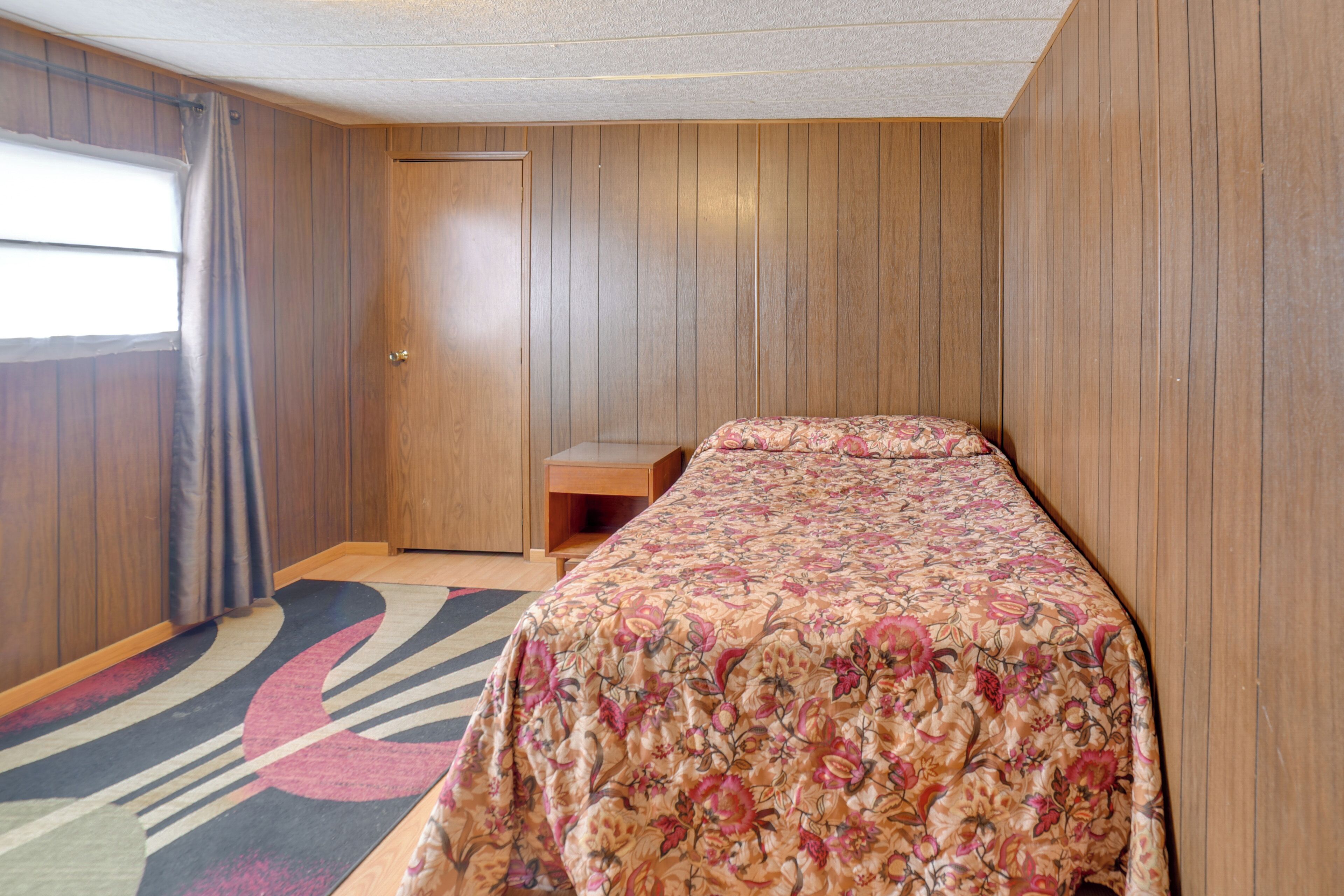 A bedroom with a bed, a wooden door, a window with curtains, and a carpet with a geometric pattern.
