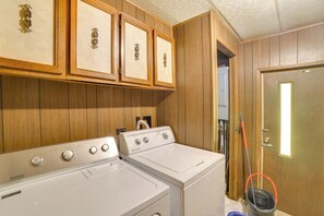 A laundry area with two white washing machines, wooden cabinets with decorative handles, and a mop leaning against the wall.