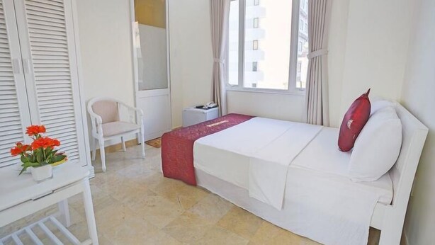 Quarto de hotel com cama, cadeira, escrivaninha, espelho e janela.