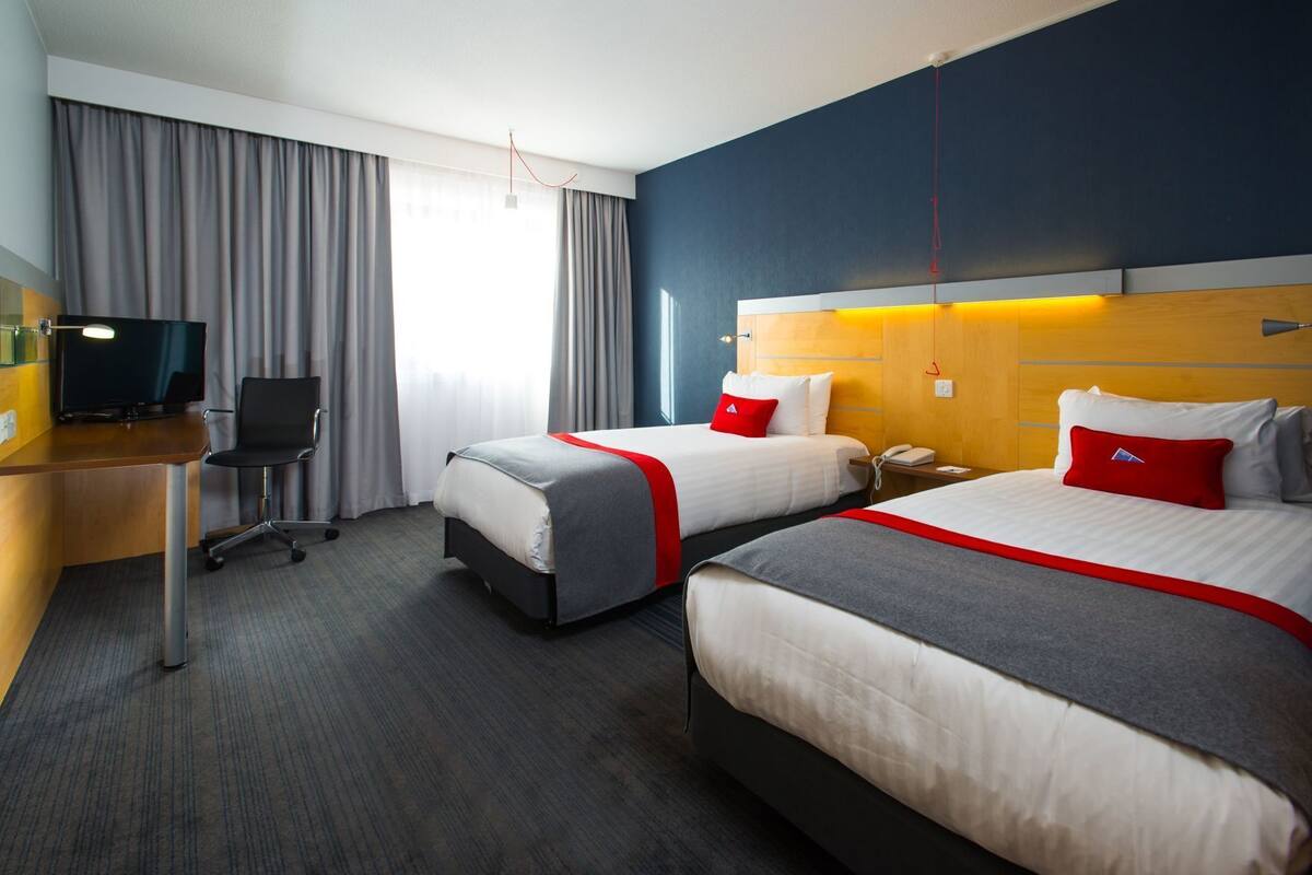 Una habitación de hotel con dos camas, un escritorio con computadora, una silla y un televisor.
