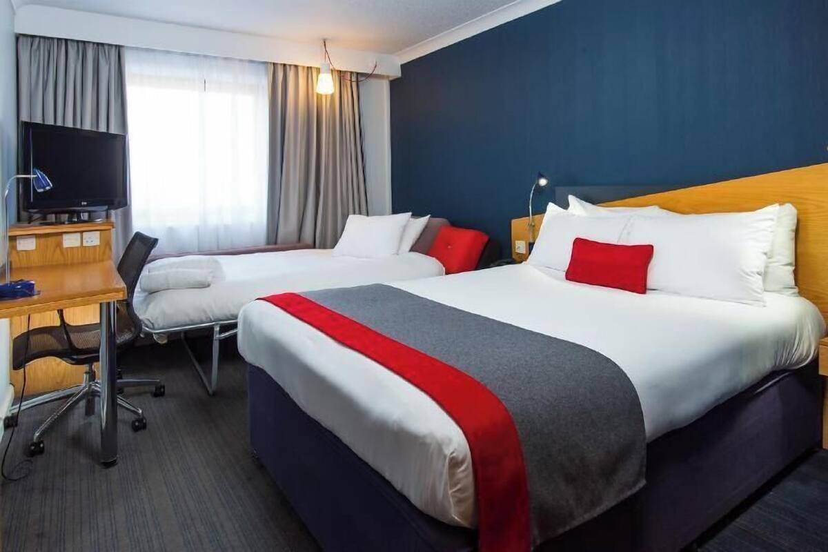 Una habitación de hotel con dos camas, un escritorio con televisor y una ventana con cortinas.
