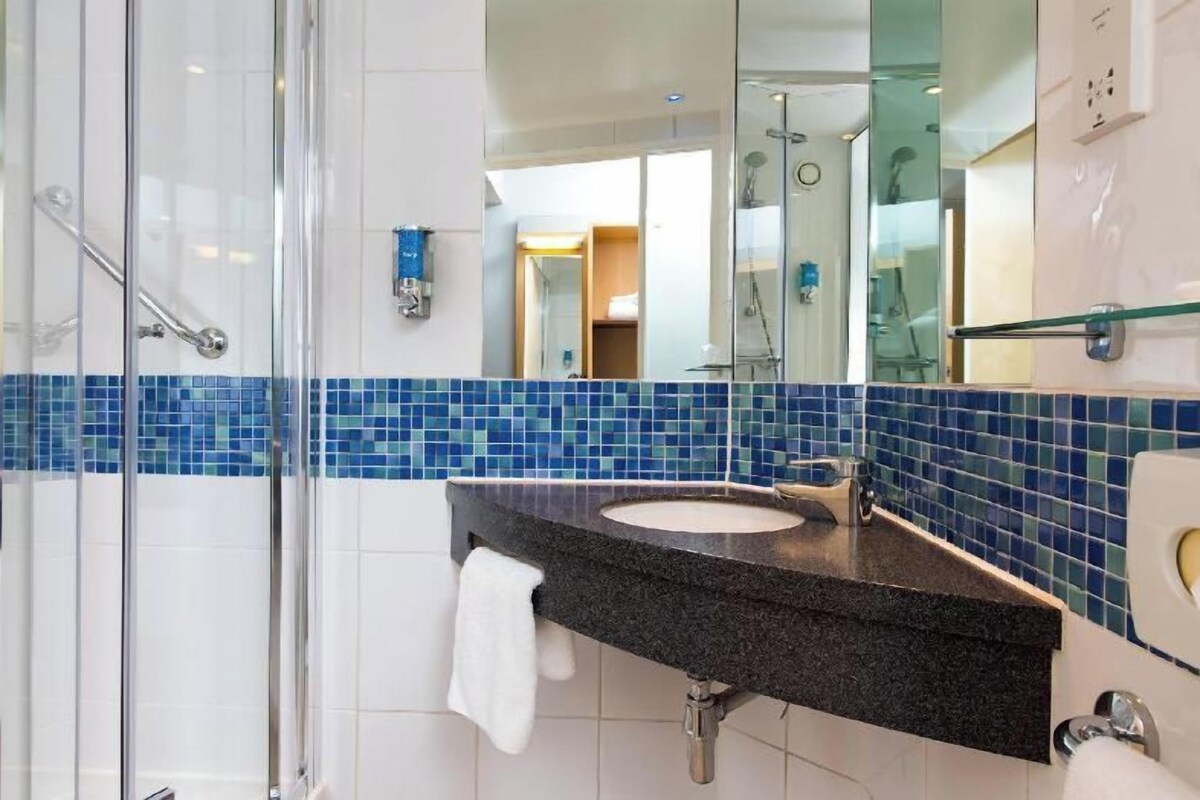 A bathroom with a glass shower enclosure, a sink with a black countertop, and blue-tiled walls.