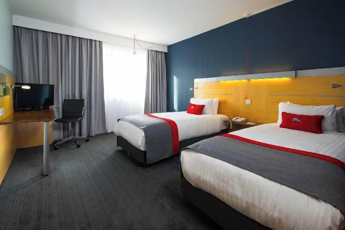 A hotel room with two beds, a desk with a TV, and a chair.