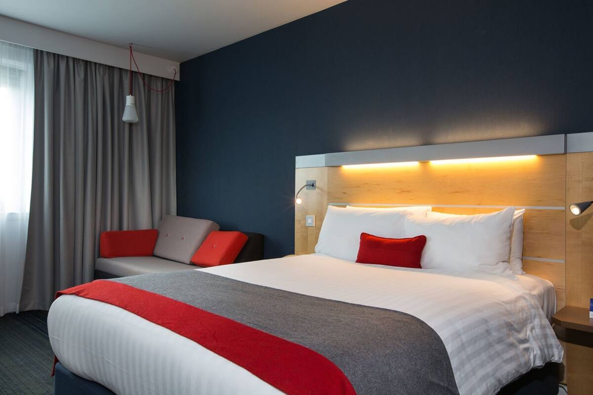 Habitación de hotel con una cama grande, un sofá, un escritorio y una ventana con cortinas.