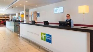 A hotel reception desk with a digital screen, a clock, and a sign indicating a hotel name. - Holiday Inn Express Newcastle City Centre (Newcastle-upon-Tyne)