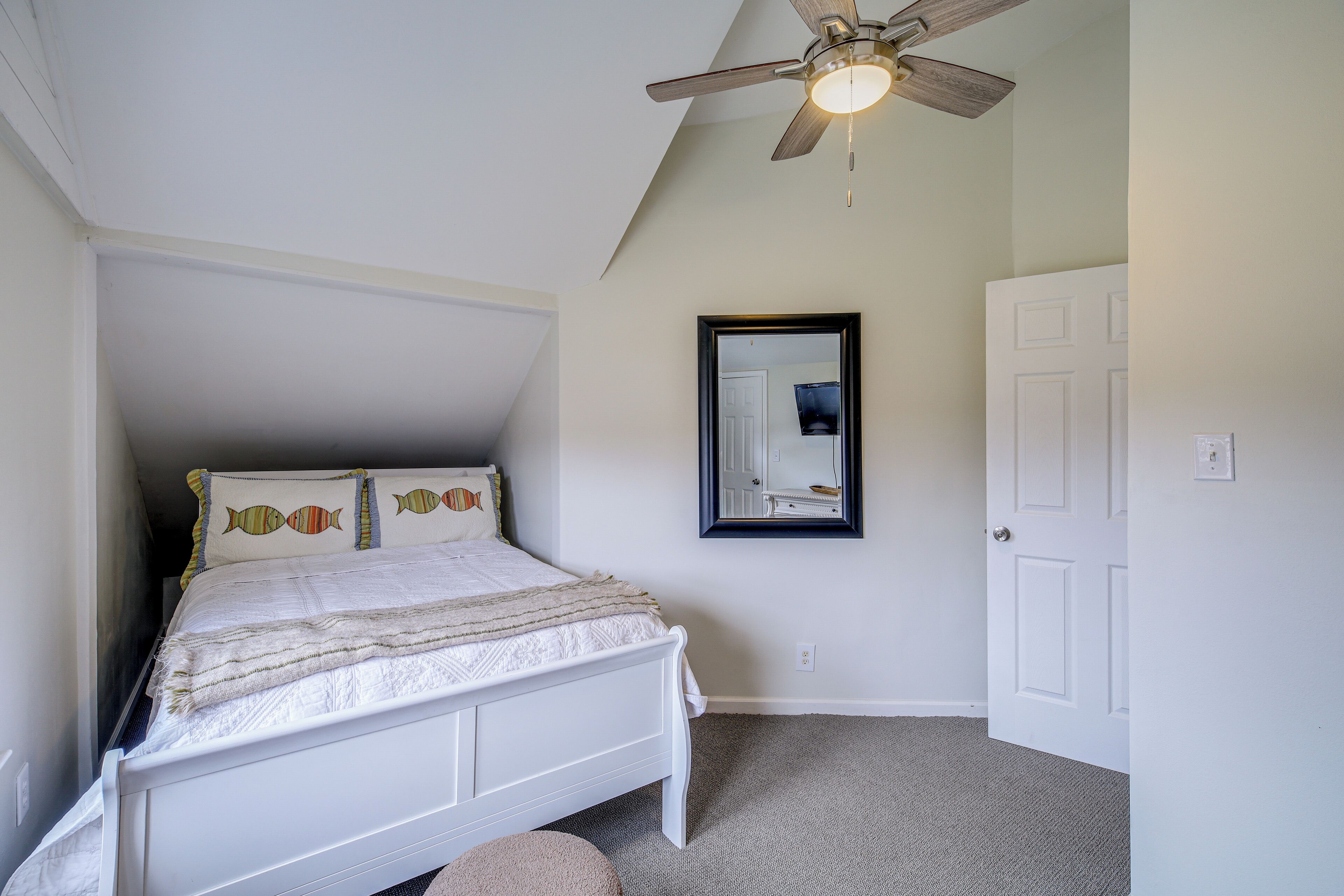 A bedroom with a white bed, a ceiling fan, a mirror, and a door.