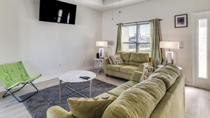 Ein Wohnzimmer mit einer Couch, einem grünen Sessel, einem Couchtisch, einem Flachbildfernseher und zwei Lampen.