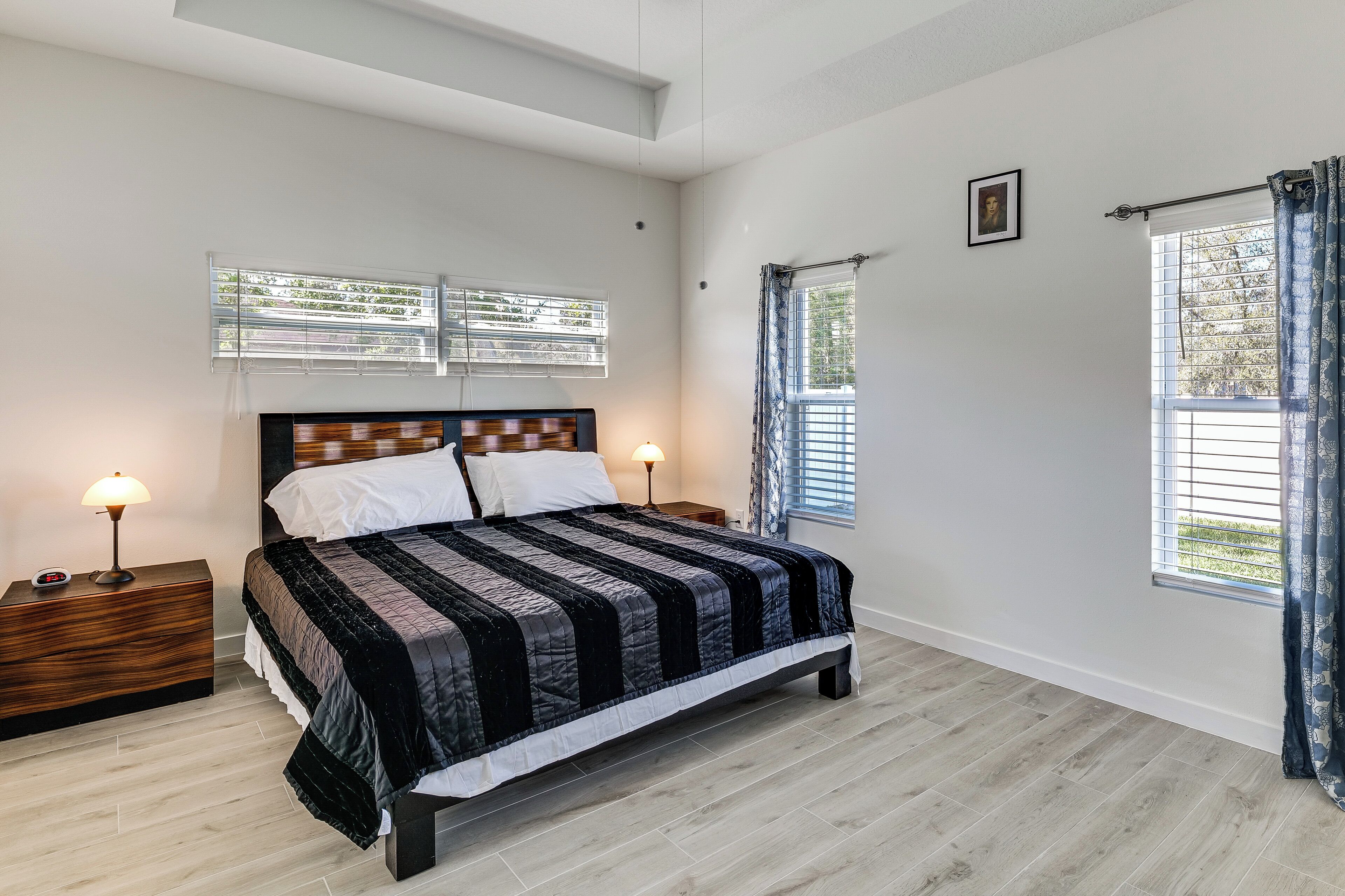 A bedroom with a bed, two bedside tables, a nightstand, a window with curtains, and a picture on the wall.