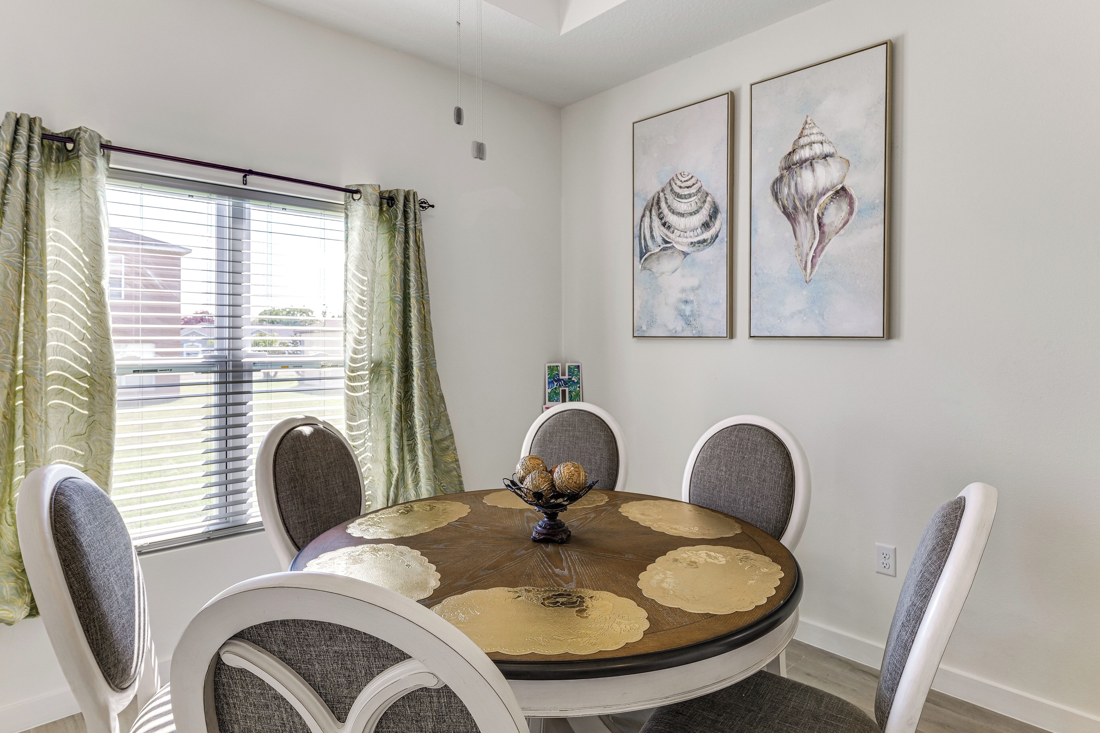 Uma sala de jantar com uma mesa redonda, cadeiras e um vaso com objetos decorativos.