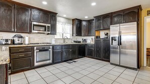 Una cucina moderna con mobili scuri, elettrodomestici in acciaio inossidabile e pavimento piastrellato.