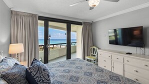 Ein Hotelzimmer mit Bett, Fernseher, Deckenventilator, Meerblick und einem Balkon.
