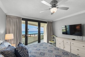 Ein Hotelzimmer mit Bett, Fernseher, Deckenventilator, Meerblick und einem Balkon.