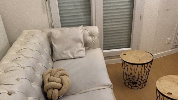 Ein helles, gestepptes Sofa mit einem runden Zierkissen und zwei kleinen runden Beistelltischen.